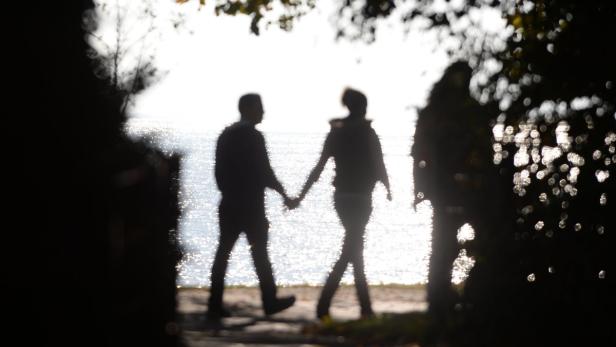 Ein Paar geht händchenhaltend am Ufer entlang, im Gegenlicht als Silhouette zu sehen.