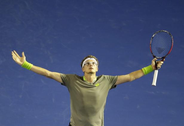 Ein Tennisspieler mit Brille und Stirnband jubelt mit erhobenen Armen und Tennisschläger.