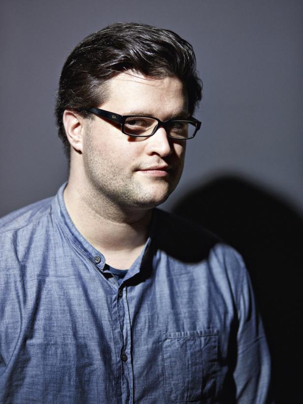 Ein Mann mit Brille und blauem Hemd blickt in die Kamera.
