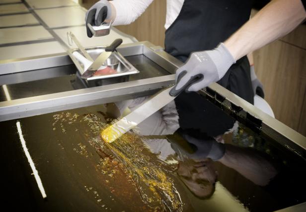 Ein Konditor verarbeitet mit Spatel und Handschuhen Karamell auf einer Metallplatte.