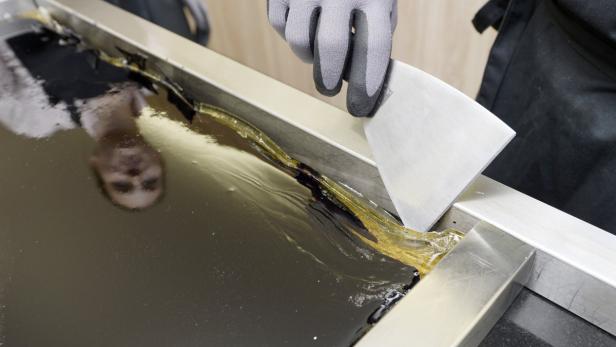 Eine Person mit Handschuhen bearbeitet flüssige Karamellbonbons mit einem Schaber.