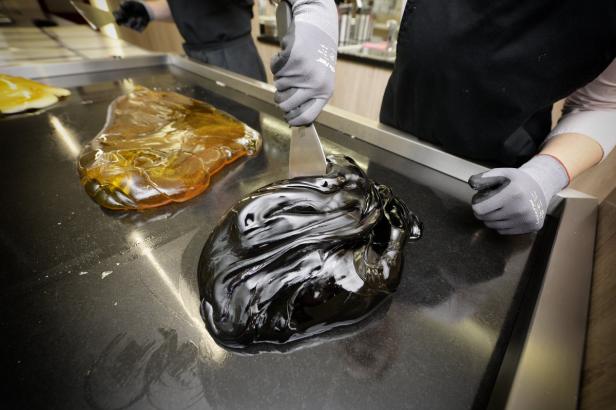 Ein Konditor bearbeitet schwarze und goldene Karamellbonbons auf einer Metallplatte.