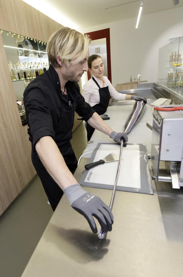 Zwei Personen formen eine lange, gestreifte Zuckerstange in einer Bonbonmanufaktur.