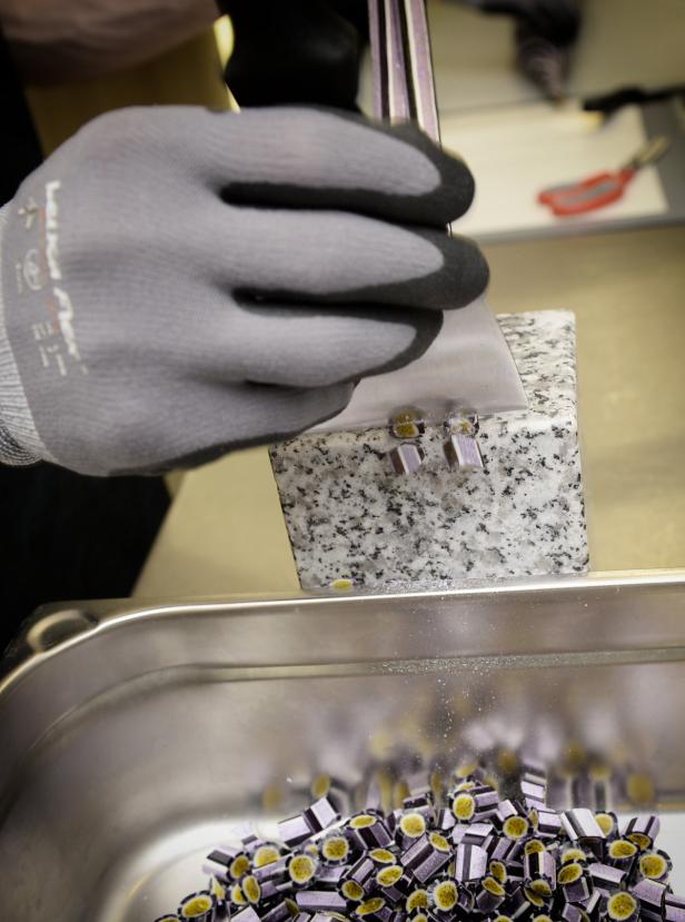 Eine Person mit Handschuhen schneidet Süßigkeiten mit einer Klinge.