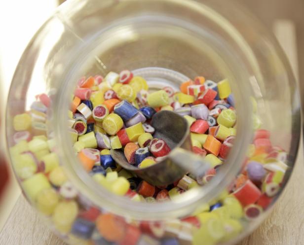 Ein Glasbehälter ist gefüllt mit bunten Bonbons und einem Löffel.