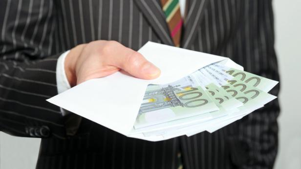 Eine Hand in einem Anzug hält einen Umschlag mit Hundert-Euro-Scheinen.