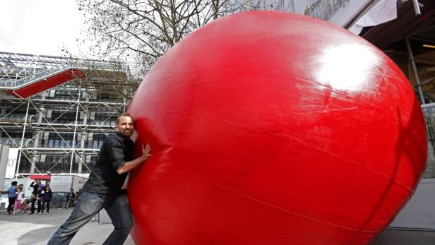 Ein Mann lehnt an einer riesigen roten Kugel vor dem Centre Pompidou in Paris.