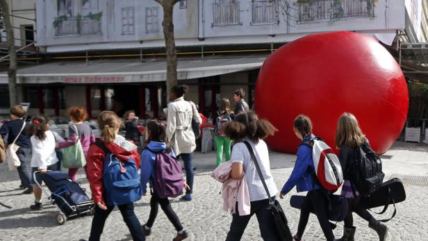 Eine Gruppe von Schulkindern geht an einem großen roten Ballon vorbei.