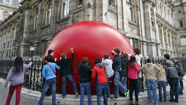 Eine Gruppe von Kindern interagiert mit einer großen, roten Kuppel vor einem Gebäude in Paris.