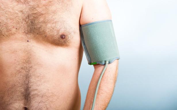 Ein Mann misst seinen Blutdruck mit einem Blutdruckmessgerät am Oberarm.