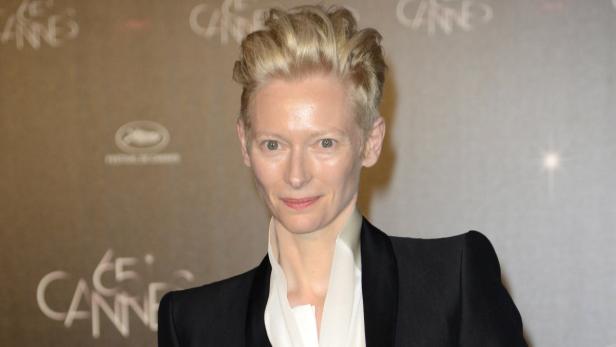 Tilda Swinton posiert vor einer Wand mit dem Schriftzug „Cannes“.