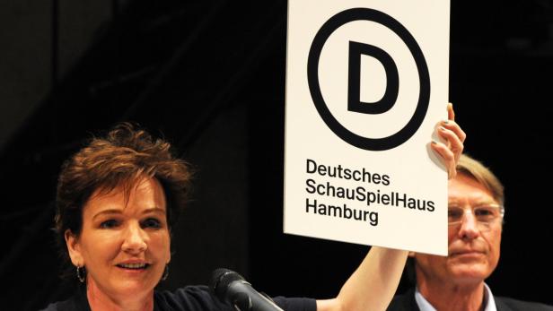 Eine Frau hält ein Schild des Deutschen Schauspielhauses Hamburg in die Höhe.