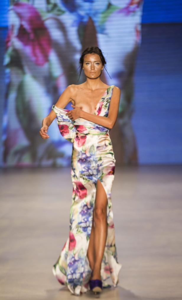 Eine Frau in einem floralen Kleid mit Schlitz läuft auf einem Laufsteg.