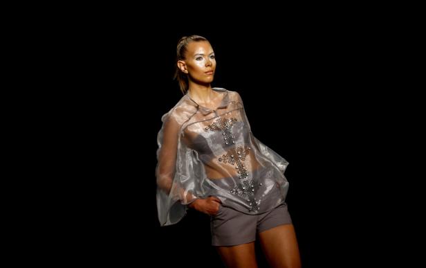 Eine Frau mit weißem Make-up präsentiert ein transparentes, silbernes Oberteil mit Verzierungen und Shorts.