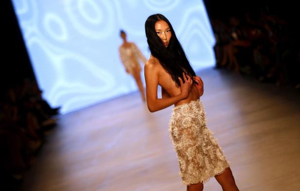 Eine Frau mit dunklen Haaren läuft in einem Rock über einen Laufsteg.