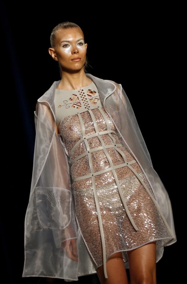 Ein Model präsentiert ein paillettenbesetztes Kleid mit transparentem Überwurf auf dem Laufsteg.