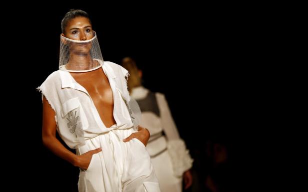 Eine Frau mit einem weißen Overall und einem futuristischen Gesichtsschutz auf einem Laufsteg.