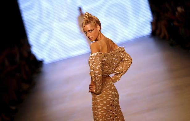 Ein Model präsentiert ein beiges, durchlöchertes Outfit auf dem Laufsteg.