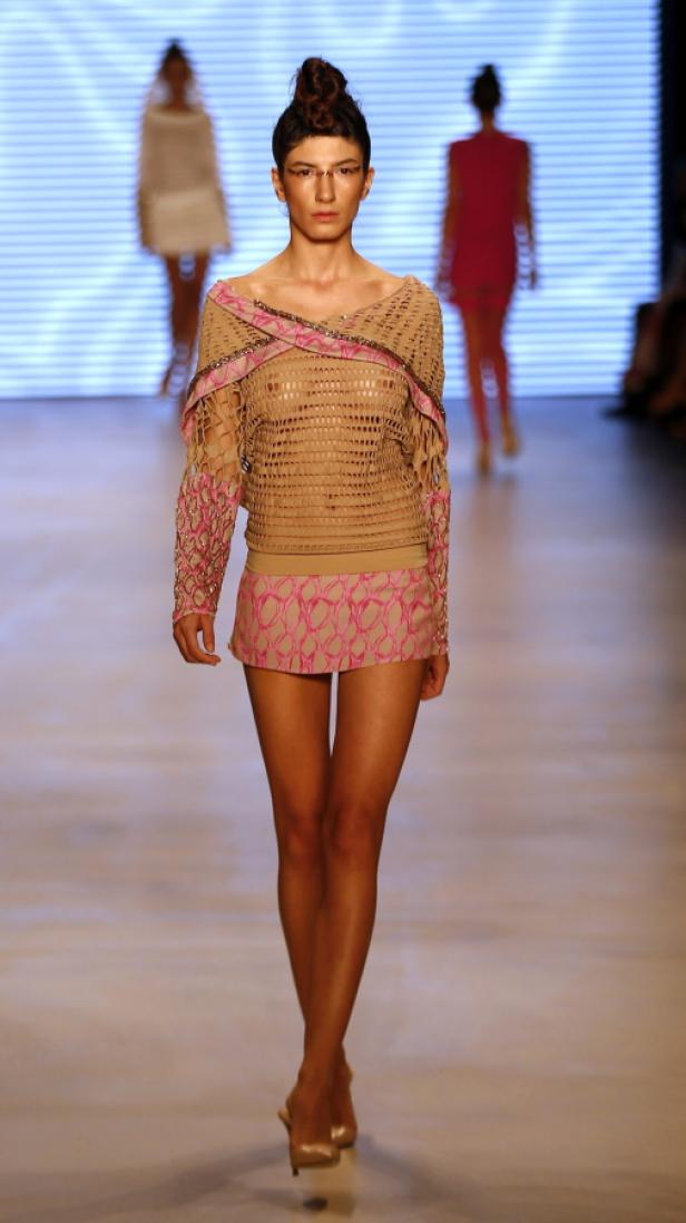 Eine Frau präsentiert ein Outfit mit Häkeloberteil und kurzem Rock auf einem Laufsteg.