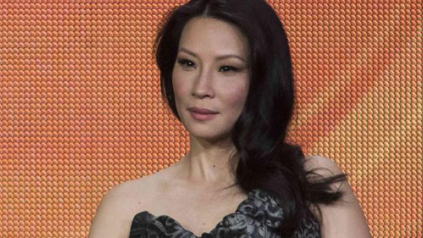 Ein Porträt von Lucy Liu vor einem orangefarbenen Hintergrund.