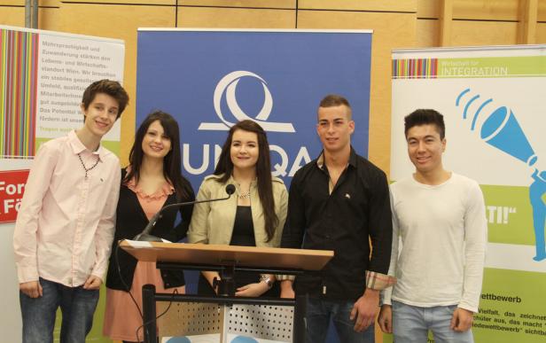 Fünf junge Menschen stehen hinter einem Rednerpult vor Bannern der Organisation UPQA.