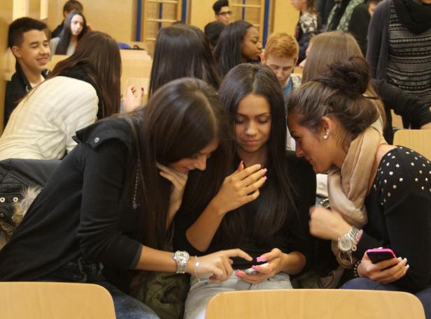 Drei junge Frauen sitzen in einem Raum und schauen auf ein Smartphone.