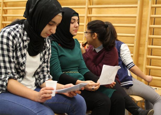 Mehrere junge Frauen sitzen und schauen auf Papiere.