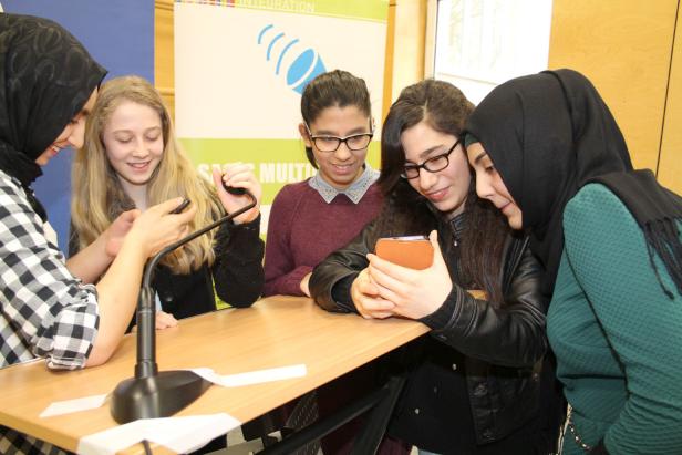 Eine Gruppe junger Frauen schaut gemeinsam auf ein Smartphone an einem Tisch.