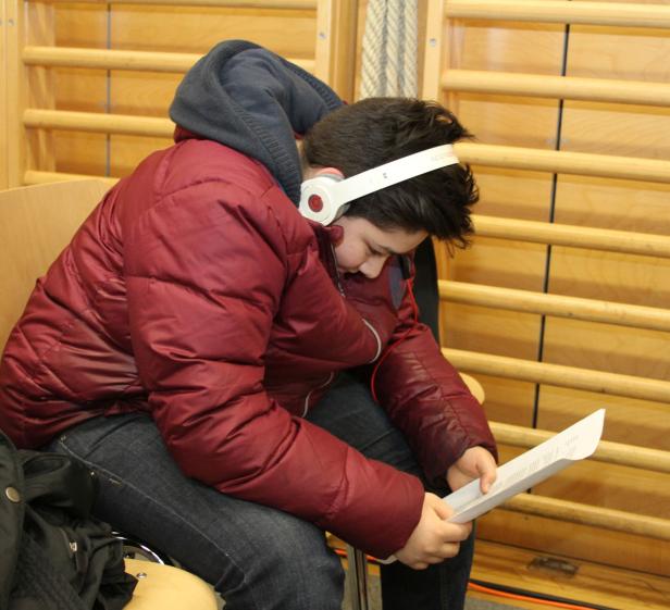 Ein Jugendlicher mit Kopfhörern liest ein Blatt Papier.