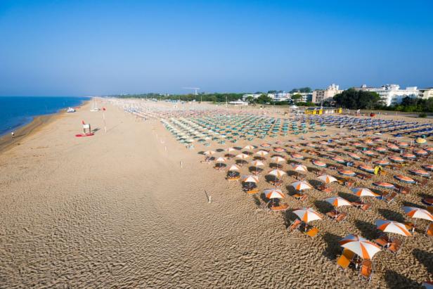 Luftaufnahme eines Strandes mit vielen Sonnenschirmen und Liegestühlen.