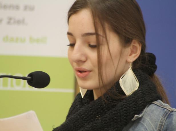 Eine junge Frau liest an einem Mikrofon vor.