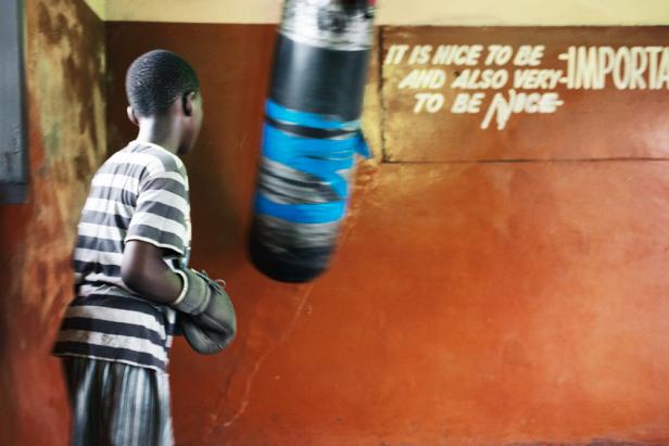 Ein junger Boxer mit Boxhandschuhen steht vor einem Boxsack in einem Raum mit einem Spruch an der Wand.