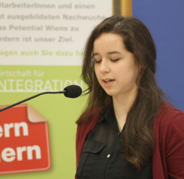 Eine junge Frau spricht bei einer Veranstaltung in ein Mikrofon.