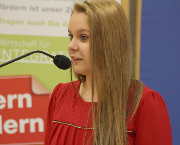 Eine junge Frau spricht bei einer Veranstaltung in ein Mikrofon.