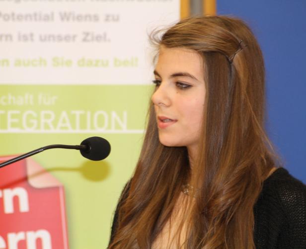 Eine junge Frau spricht bei einer Veranstaltung in ein Mikrofon.