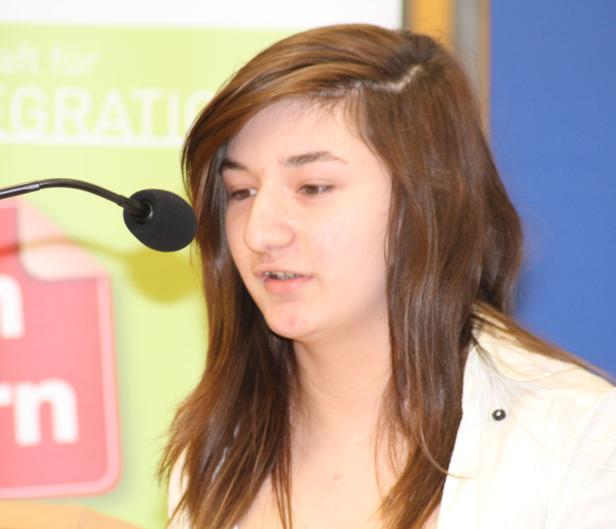 Eine junge Frau spricht bei einer Veranstaltung in ein Mikrofon.