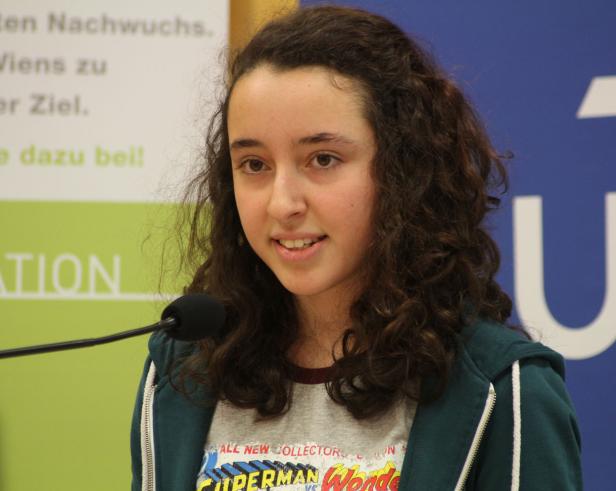 Ein junges Mädchen mit lockigem Haar spricht an einem Mikrofon.