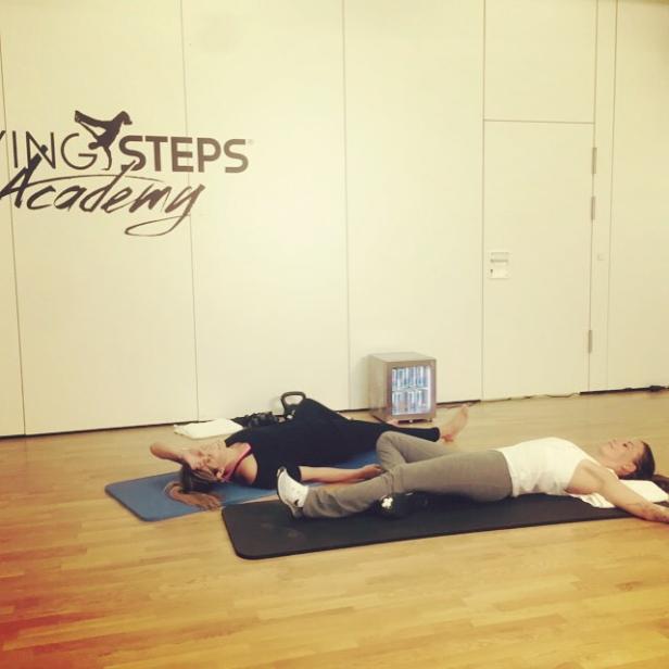Zwei Frauen liegen entspannt auf Yogamatten in einem Fitnessstudio.