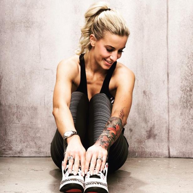Eine Frau mit Tattoo sitzt in Sportkleidung auf dem Boden.