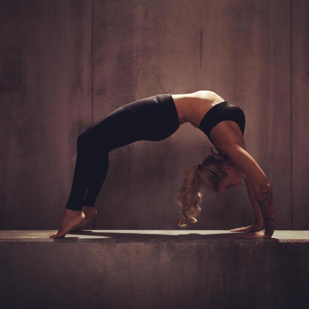 Eine Frau macht eine Yoga-Übung in Sportkleidung vor einer grauen Wand.