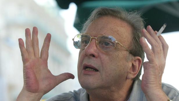 Ein Mann mit Brille gestikuliert und hält eine Zigarette in der Hand.