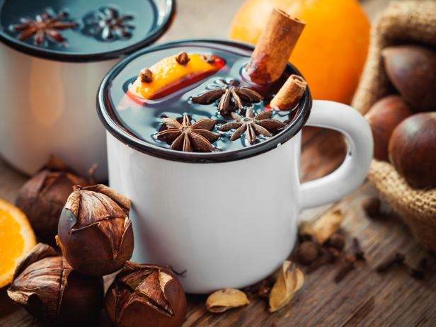 Glühwein mit Sternanis, Orange und Zimtstange in weißen Tassen auf einem Holztisch.
