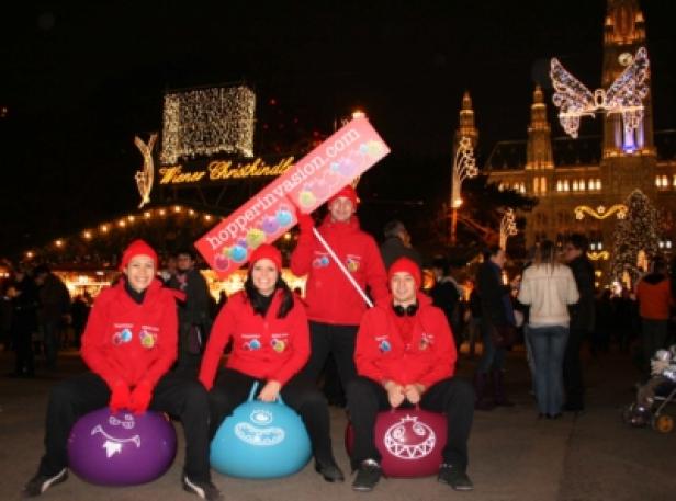 Sony Ericsson-Hopper Invasion/CGK Communication Group Vier Personen auf Hüpfbällen vor dem Wiener Christkindlmarkt mit einem „hopperinvasion.com“-Schild.
