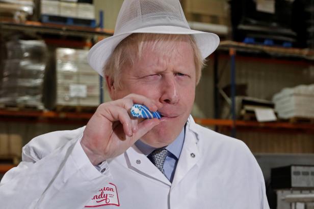 Boris Johnson isst ein blau-weißes Bonbon in einer Süßwarenfabrik.