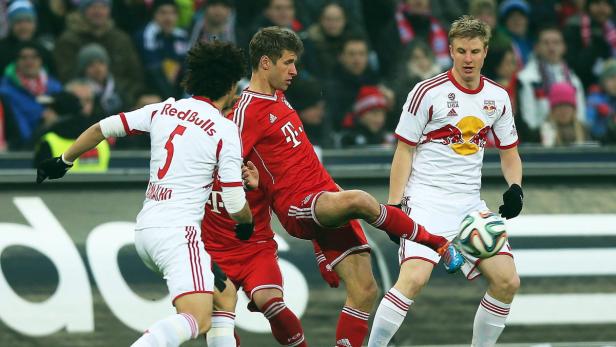 Thomas Müller (im roten Trikot) spielt Fußball gegen zwei Gegenspieler.