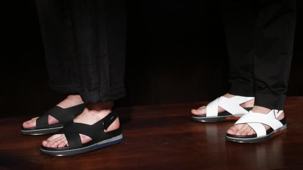 Models present creations from Jimmy Choo during it Zwei Personen tragen schwarze und weiße Sandalen mit gekreuzten Riemen.