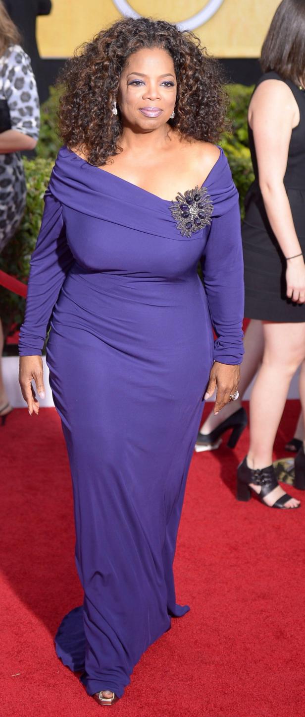 Oprah Winfrey in einem lilafarbenen Kleid auf einem roten Teppich.