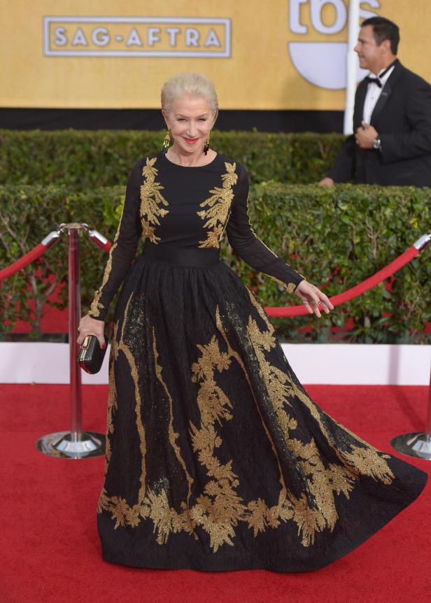 Helen Mirren in einer langen, schwarzen Robe mit goldenen Verzierungen auf dem roten Teppich.