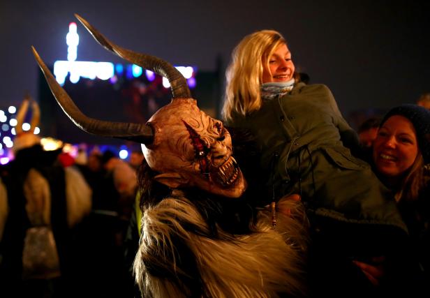 A person costumed as Krampus or Percht, figures from ancient Austrian custom, lifts a young spectator during a Perchten run in Vienna