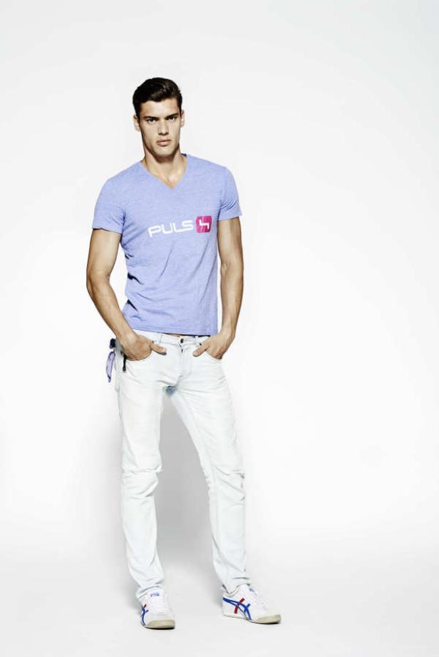 Ein Mann in Jeans und T-Shirt posiert vor einem weißen Hintergrund.